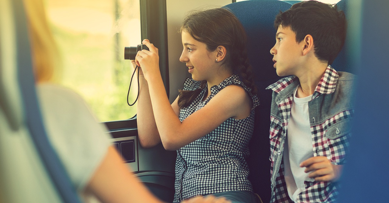 Mädchen macht Foto mit Digitalkamera aus dem Zug heraus, Junge schaut ihr über die Schulter